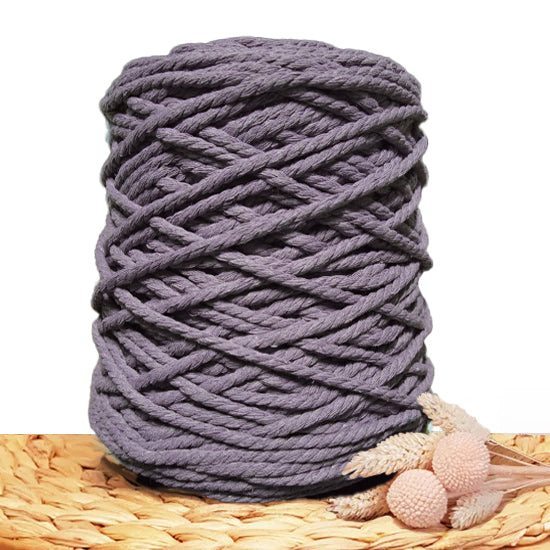 A large roll of 5mm twisted cord in a muted dark grey blue color, styled on a woven straw mat with dried decorative grasses against a white background.