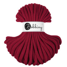A skein of chunky braided cord in deep burgundy, wrapped with a white paper label that reads 'Bobbiny'.