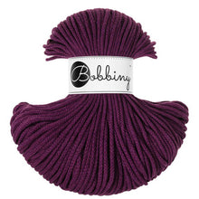 A skein of Bobbiny braided cord in a deep plum purple color, featuring a white paper label with the brand name 'Bobbiny' in black script and logo, set against a plain white background.