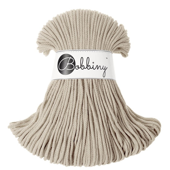 A skein of light beige braided cord with a white paper band in the center featuring the black script logo 'Bobbiny'.