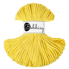 A skein of bright yellow braided cord  with a white paper label in the center that reads 'Bobbiny' in black script and logo, photographed on a plain white background.