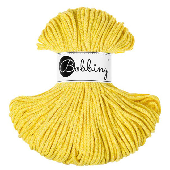 A skein of bright yellow braided cord  with a white paper label in the center that reads 'Bobbiny' in black script and logo, photographed on a plain white background.