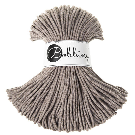 A skein of coffee coloured braided cord wrapped with a white paper band labeled 'Bobbiny' in black script and logo, set against a plain white background.