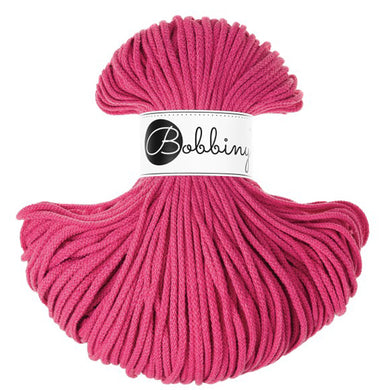 A skein of bright pink braided cord with a white paper label in the center that reads 'Bobbiny' in black script and logo, set against a plain white background.