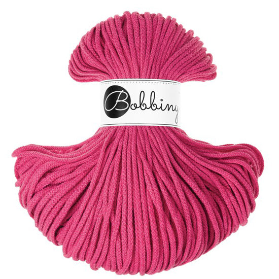 A skein of bright pink braided cord with a white paper label in the center that reads 'Bobbiny' in black script and logo, set against a plain white background.
