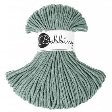A skein of laurel green braided cord with a white paper label in the center that reads 'Bobbiny'.