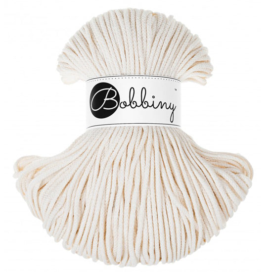 A skein of Bobbiny brand cotton cord in a warm cream color, wrapped with a white paper label featuring the black 'Bobbiny' logo, set against a plain white background.