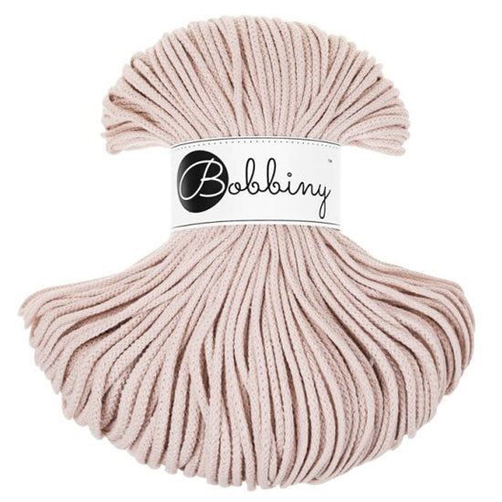 A skein of Bobbiny braided cord in a soft pink or nude shade featuring a white paper label with the brand name 'Bobbiny' in black script. The yarn is arranged in a rounded, fan-like shape against a solid white background.