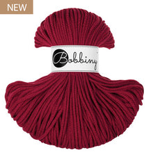 A skein of Bobbiny yarn in a deep red color, featuring a white paper label with the brand name 'Bobbiny' in black script. A small brown 'NEW' label is in the top-left corner.