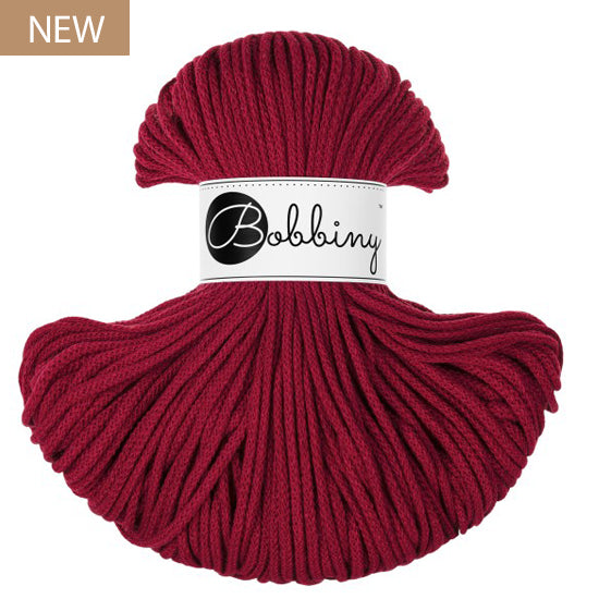 A skein of Bobbiny yarn in a deep red color, featuring a white paper label with the brand name 'Bobbiny' in black script. A small brown 'NEW' label is in the top-left corner.