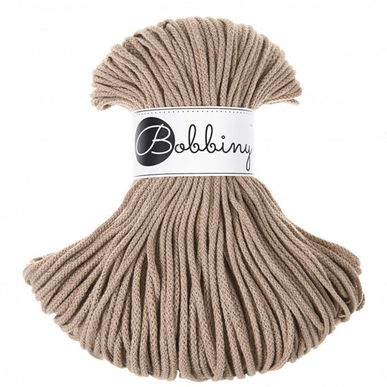 A skein of Bobbiny braided cord in a warm taupe-beige color, wrapped with a white paper label featuring the brand name 'Bobbiny' in black script and logo, set against a plain white background.