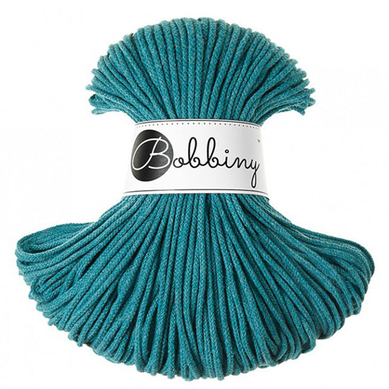 A skein of teal braided cord with a white paper label wrapped around the middle that reads 'Bobbiny'.