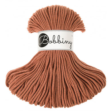 A skein of Bobbiny braided cord in a warm terracotta color, featuring a white paper label with the brand name 'Bobbiny' in black script, set against a plain white background.