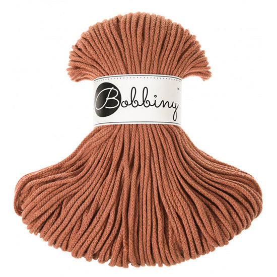 A skein of Bobbiny braided cord in a warm terracotta color, featuring a white paper label with the brand name 'Bobbiny' in black script, set against a plain white background.