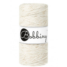 A spool of Bobbiny cotton cord in a cream color with gold thread, featuring a white paper label with the black 'Bobbiny' logo, set against a plain white background.