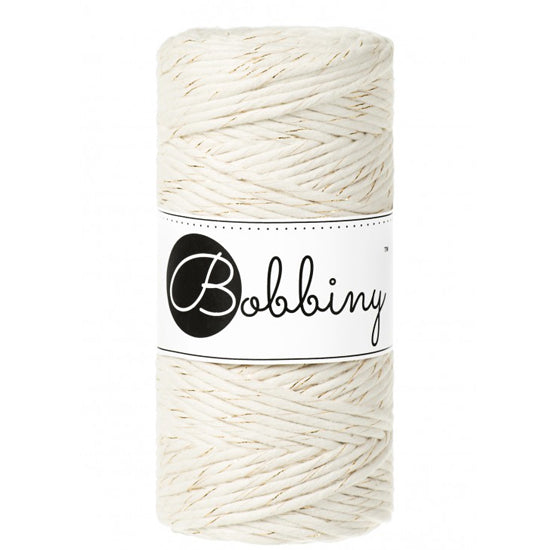 A spool of Bobbiny cotton cord in a cream color with gold thread, featuring a white paper label with the black 'Bobbiny' logo, set against a plain white background.