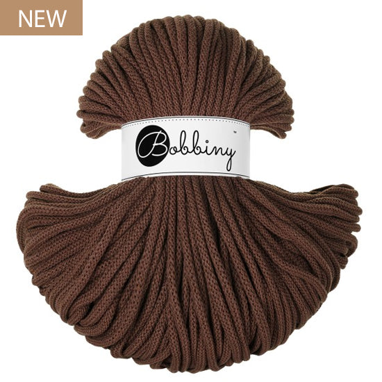 A skein of Bobbiny braided cord in a rich brown color, wrapped with a white paper band displaying the brand name 'Bobbiny'. A small tan 'NEW' label is in the top-left corner.