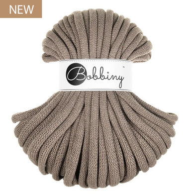 A skein of chunky braided cord in a coffee or taupe, wrapped with a white paper band featuring the 'Bobbiny' brand logo. A small brown 'NEW' label is in the top-left corner.
