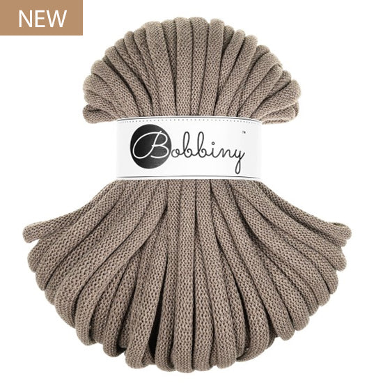 A skein of chunky braided cord in a coffee or taupe, wrapped with a white paper band featuring the 'Bobbiny' brand logo. A small brown 'NEW' label is in the top-left corner.