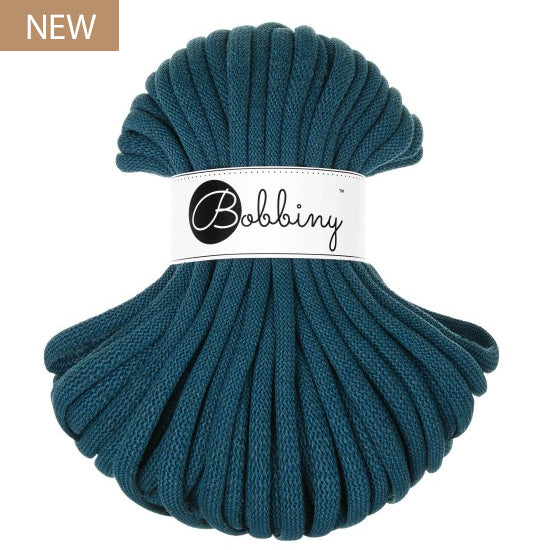 A skein of thick braided cord in a deep teal blue-green color, wrapped with a white paper band featuring the 'Bobbiny' brand logo. A small brown 'NEW' label is in the top-left corner.