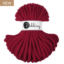 A skein of chunky braided cord in a deep burgundy red color, wrapped with a white paper band featuring the 'Bobbiny' brand logo. A small brown 'NEW' label is in the top-left corner.