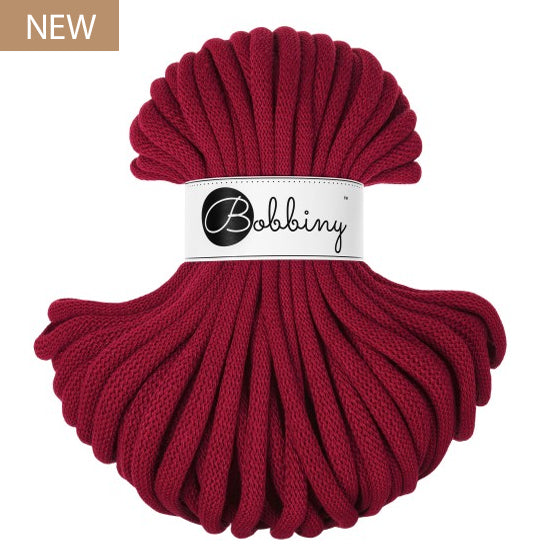 A skein of chunky braided cord in a deep burgundy red color, wrapped with a white paper band featuring the 'Bobbiny' brand logo. A small brown 'NEW' label is in the top-left corner.