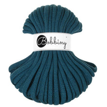 A coiled skein of thick braided cord in a deep teal blue-green color, wrapped with a white paper band featuring the black script logo 'Bobbiny'.