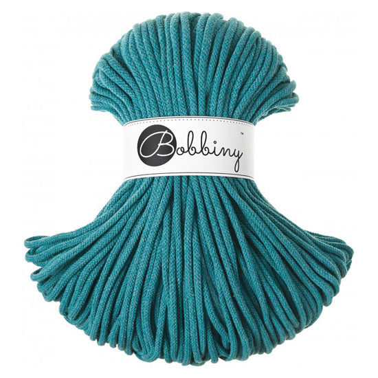 A skein of teal 5mm braided rope or cord with a white paper label wrapped around the center that reads 'Bobbiny'.